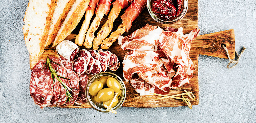 Meat appetizer selection or wine snack set. Variety of smoked meat, salami, prosciutto, bread sticks, baguette, olives and sun-dried tomatoes on rustic wooden board, top view, horizontal